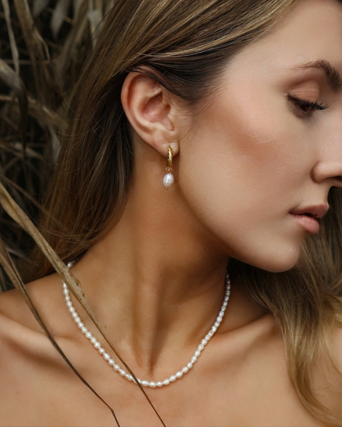 Close-up of a woman wearing a pearl necklace and earring with a blurred natural background