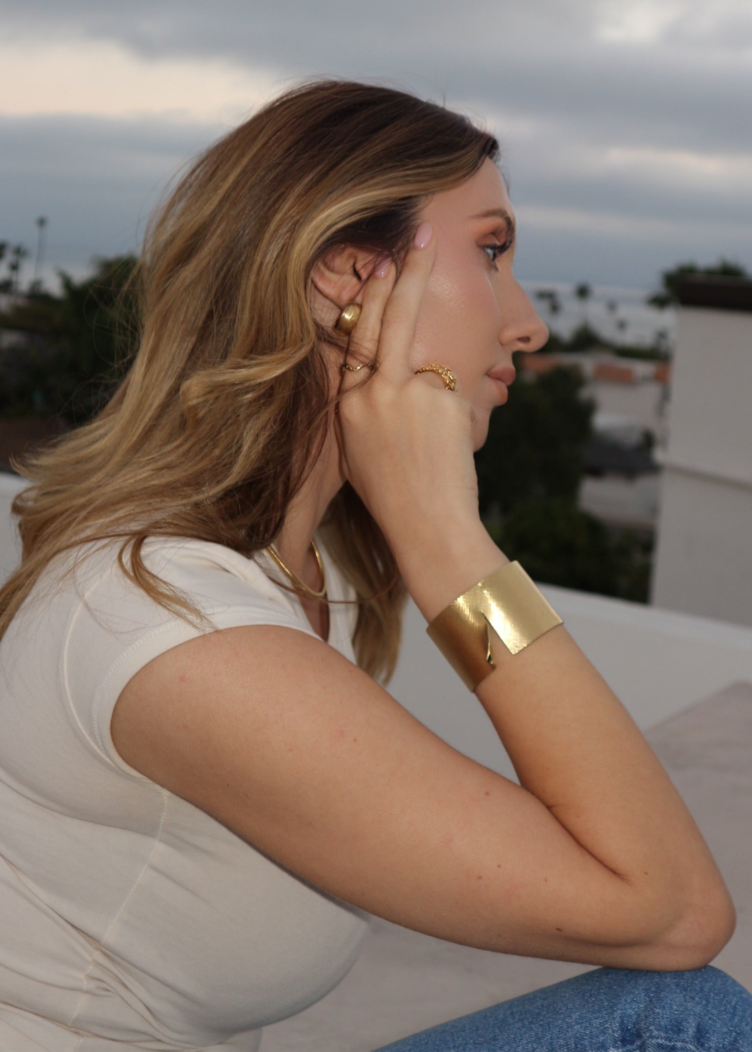 Woman wearing gold jewelry outdoors with a blurred background