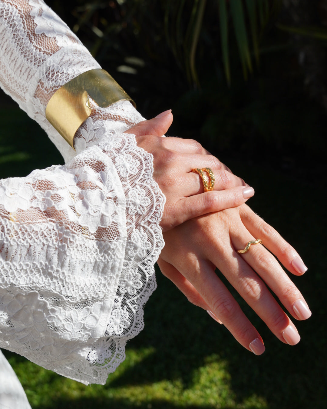 Close-up of hands with rings on fingers, wearing lace gloves against a blurred natural background