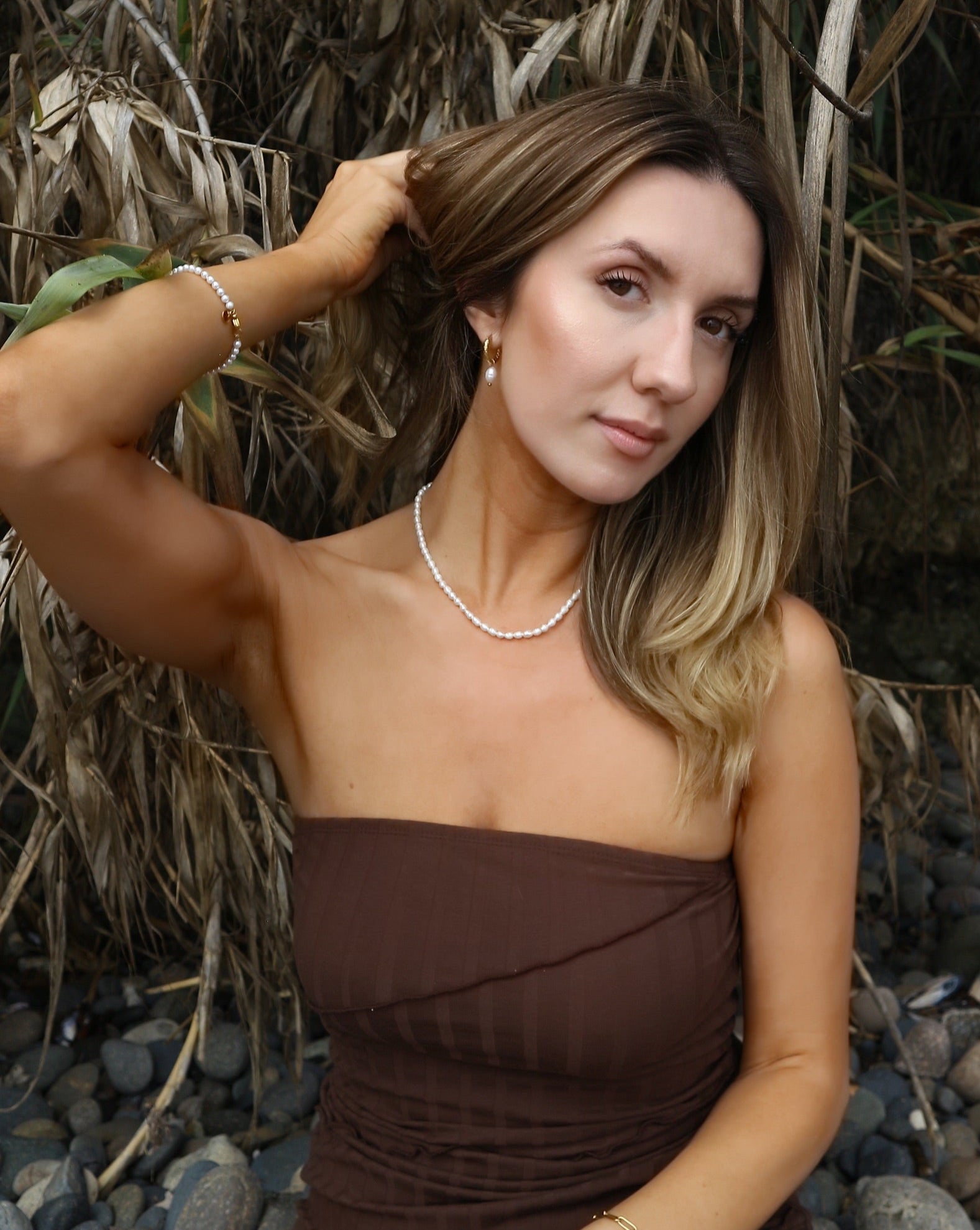 Woman in a brown dress sitting on pebbles with plants in the background
