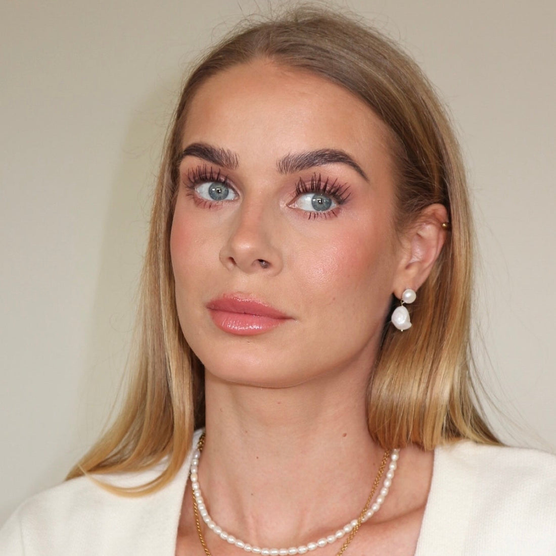 Woman wearing pearl jewelry against a neutral background