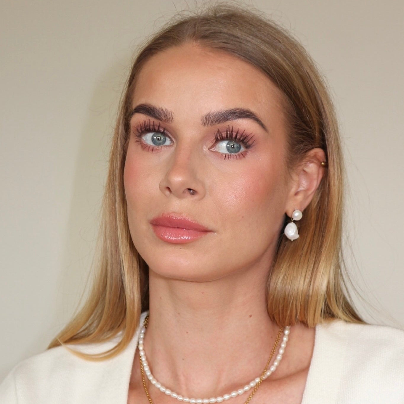 Woman wearing pearl jewelry against a neutral background