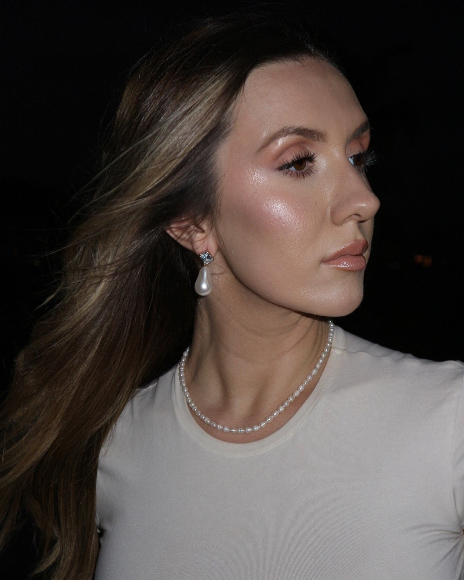 Woman wearing a pearl necklace and earrings against a dark background