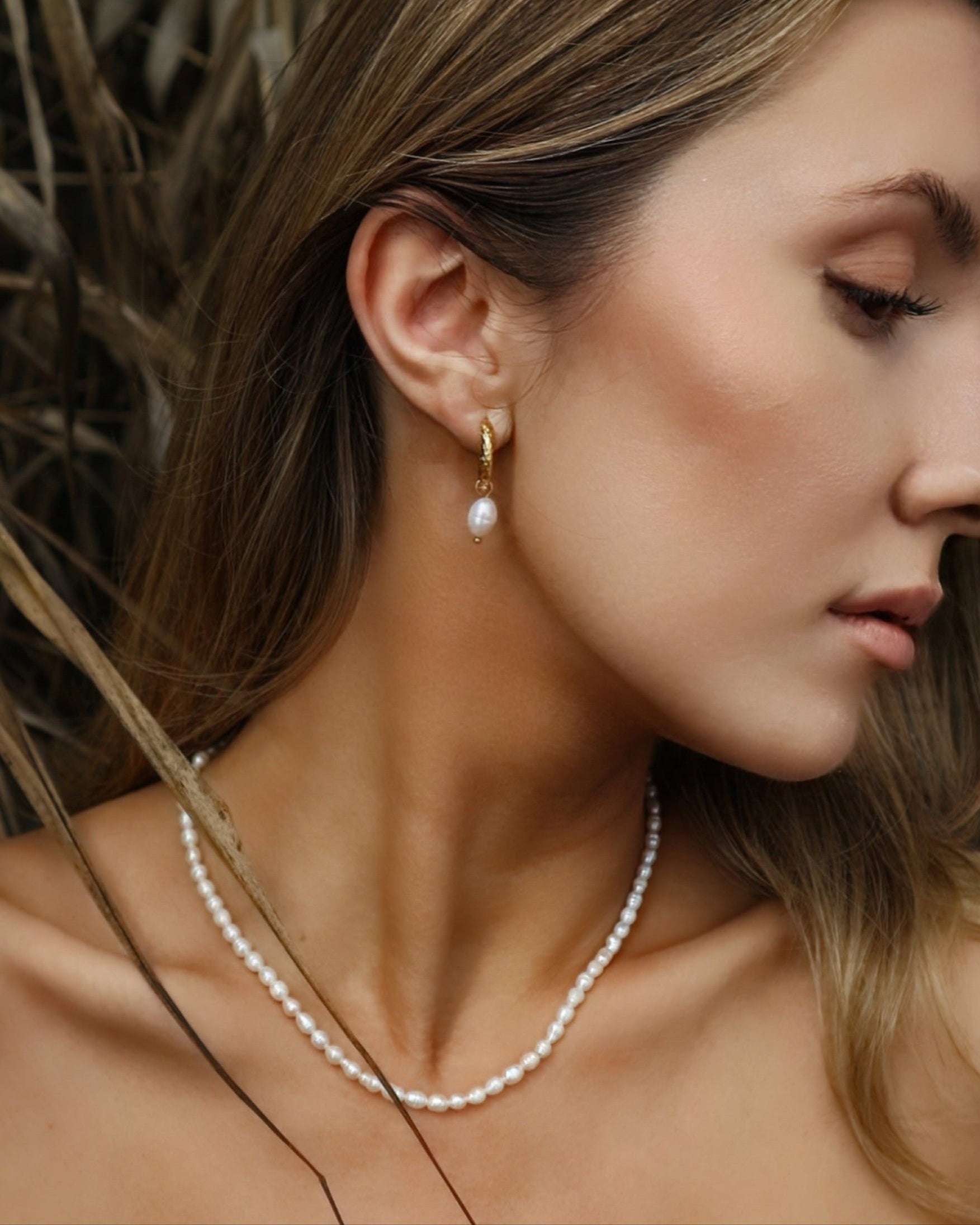 Close-up of a woman wearing a pearl necklace and earring with a blurred natural background