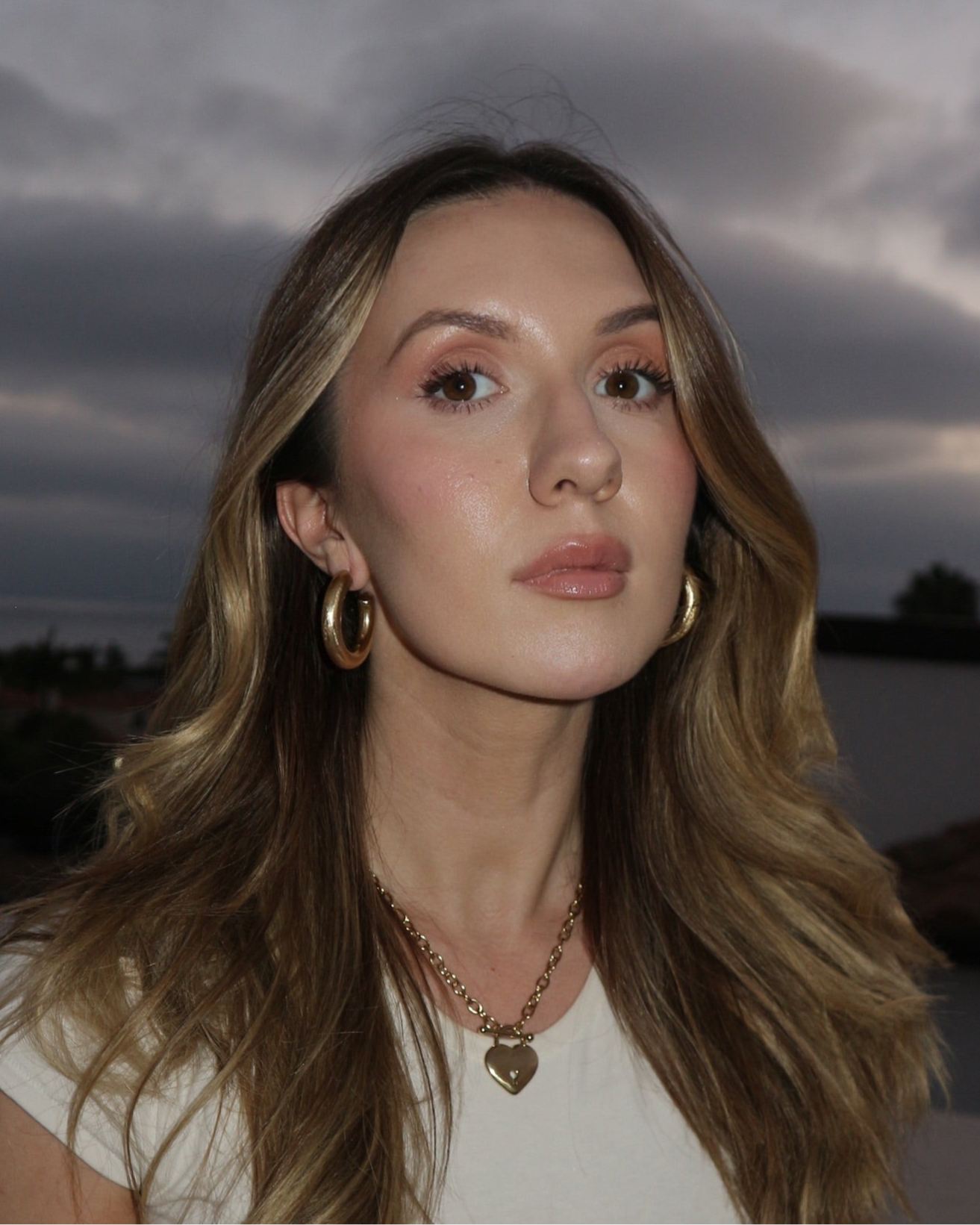 Woman with long hair and gold earrings against a dark sky