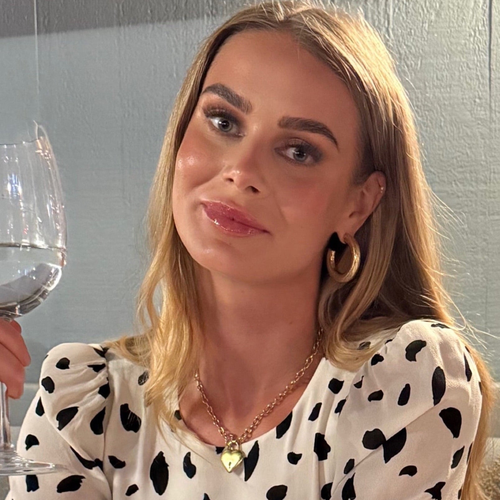 Woman in a polka dot blouse holding a glass of wine indoors.