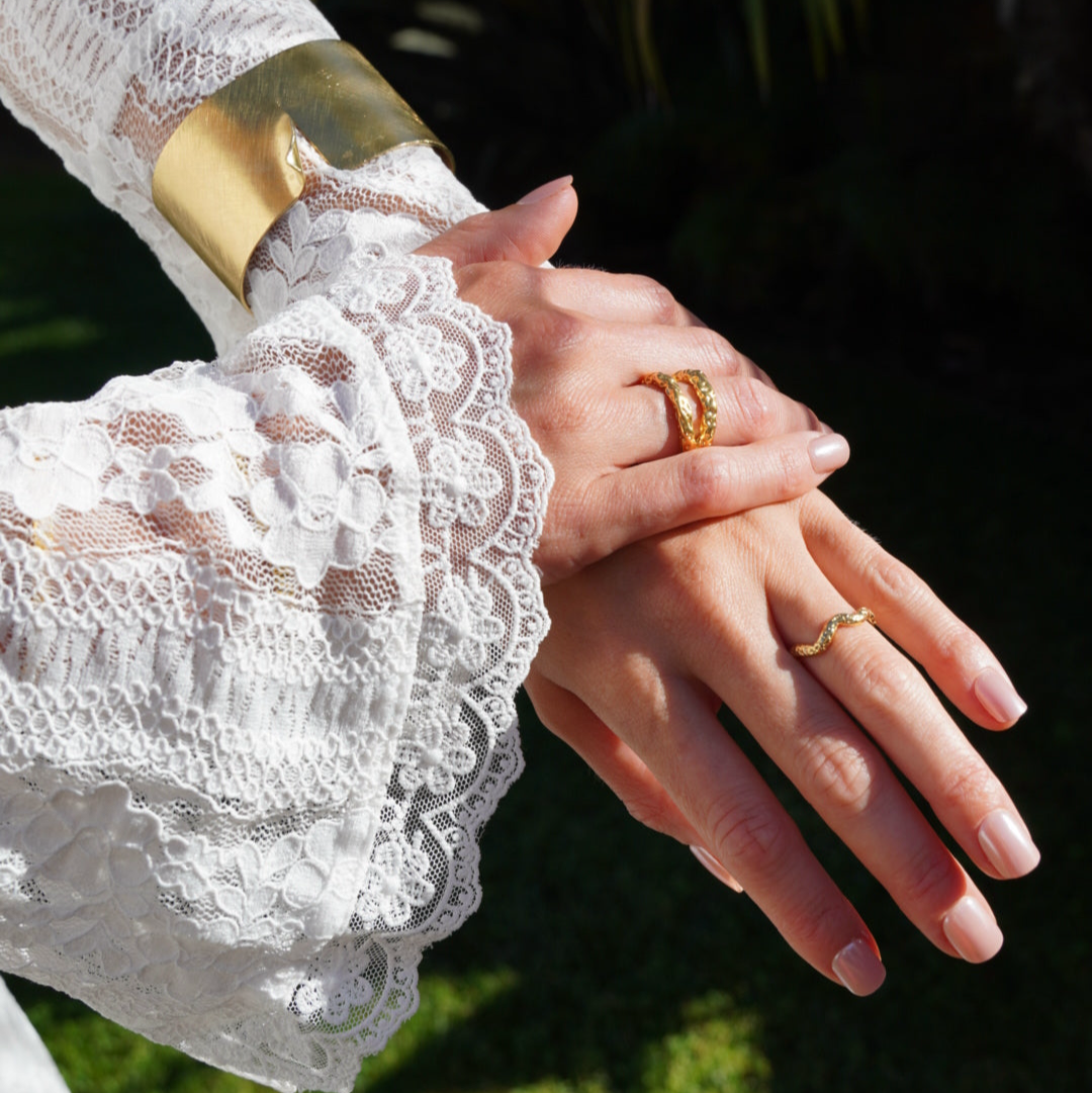 Close-up of hands wearing gold rings with lace-trimmed sleeves against a blurred natural background